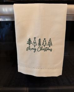 a kitchen towel hanging on the oven door with merry christmas trees embroidered on it, in front of an oven