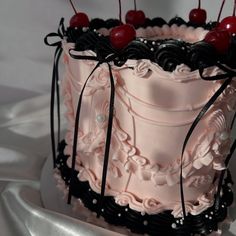 a pink and black decorated cake with cherries on it's top, sitting on a white table cloth