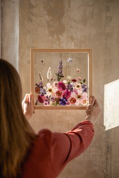 a woman holding up a painting with flowers in it