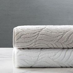 two white towels stacked on top of each other in front of a gray wall and floor