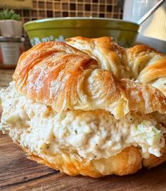 a croissant with chicken salad on it sitting on top of a wooden table