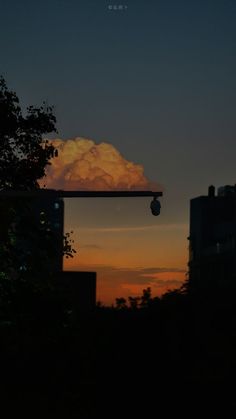 the sun is setting over some buildings and trees in front of a cloud filled sky