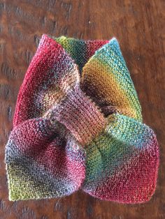 a multicolored knitted bow on top of a wooden table next to a pair of scissors