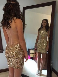 a woman standing in front of a mirror wearing a dress with gold sequins