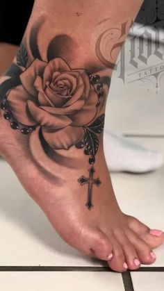 a woman's foot with a rose and cross tattoo on the top of it