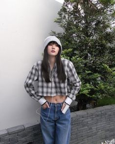 a young woman standing in front of a white wall wearing headphones and a plaid shirt