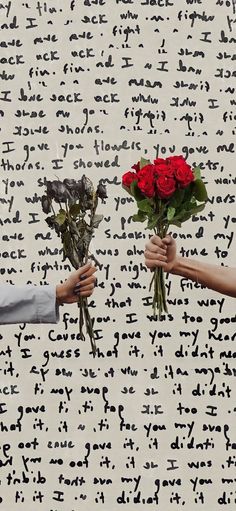 two people holding flowers in front of a wall with writing on it and one person handing the roses to each other