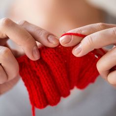 the woman is knitting her red knitted armwarf with one hand and two fingers