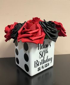 a white box with black and red flowers in it sitting on a table next to a wall