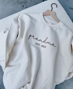 Indulge in cozy lounge wear with the Custom Embroidered Cursive Mama Grandma Nana Gigi Sweatshirt! This holiday season, show your family and friends some love with this personalized gift. The cursive embroidery adds a touch of elegance to this comfortable and stylish pullover. Perfect for Christmas and Thanksgiving, or any day you want to feel extra special! Product Details -Our unisex sweatshirts are crafted from 50% cotton and 50% polyester, ensuring comfort and durability. Please note that ou Grandma Embroidered Sweatshirt, White Custom Embroidered Tops For Loungewear, Relaxed Fit Sweater With Letter Embroidery For Loungewear, Loungewear Sweater With Letter Embroidery And Relaxed Fit, Cozy White Embroidered Sweatshirt, Gigi Sweatshirt, Nana Sweatshirt, Cozy Lounge, Short Words