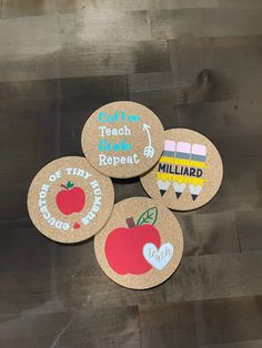 four cork coasters with different designs on them sitting on a wooden floor in front of a wall