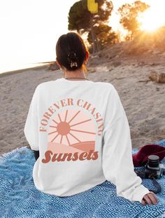 Stay stylish and cozy in the Forever Chasing Sunsets sweatshirt, a retro beach sweater with oversized aesthetic perfect for summer vibes. This trendy boho sunset pullover hoodie is a must-have for those who love chasing sunsets in style. ABOUT THE SWEATSHIRT - Gildan 18000 -50% cotton, 50% polyester -Size chart is true to size; if you would like the oversized style size up 1-3 sizes -Wash Inside Out In Cold Water SHIPPING AND PROCESSING All sweatshirts are processed and shipped within 1-7 busine Vsco Graphic Print Sweatshirt For Beach Season, Vsco Style Sweatshirt With Letter Print For Vacation, Oversized Graphic Print Sweatshirt For Beach Season, Vsco Letter Print Sweatshirt For Beach, Vsco Relaxed Fit Sweatshirt For Vacation, Relaxed Fit Vsco Sweatshirt For Vacation, White Long Sleeve Sweater For Beach Season, Oversized Graphic Print Sweatshirt For Vacation, Oversized Crew Neck Sweatshirt For Beach