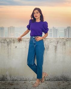 a woman standing on top of a cement wall with her hands in her pockets and looking at the camera