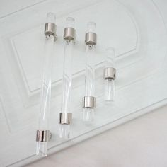 four clear glass tubes sitting on top of a white counter next to a silver object