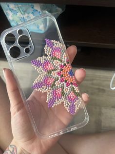 a person holding up a phone case with beads on the front and back of it