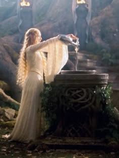 a woman in white dress standing next to a fountain