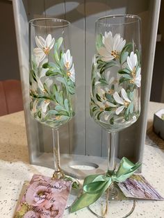 two wine glasses sitting on top of a table next to each other with flowers painted on them