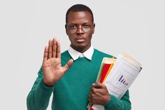 a man in green sweater holding papers and making stop sign with his hand while wearing glasses