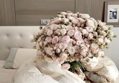 a bouquet of pink roses sitting on top of a white bed next to pillows and blankets