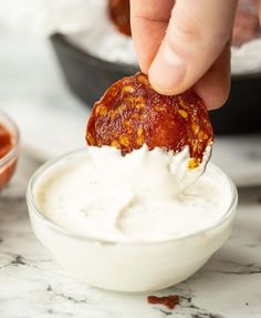 a person dipping something into a small bowl with sauce in it on a marble countertop