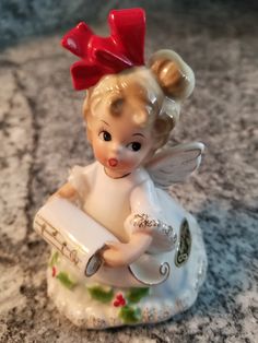 a little angel figurine with a red bow holding a book on top of a table