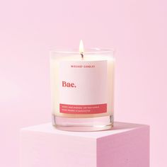 a candle sitting on top of a block of pink paper with the word bae printed on it