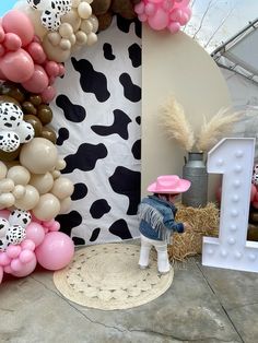 there is a fake cow standing in front of the balloon wall with balloons on it