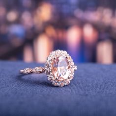 an oval shaped diamond ring on top of a blue cloth with blurry lights in the background