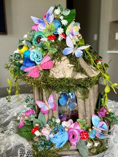 a small birdhouse with flowers and butterflies on it's roof, sitting on a lace tablecloth