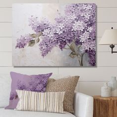 a living room with a white couch and purple flowers on the wall above it is a lamp