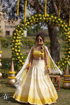 a woman in a yellow and white dress standing under a tree with flowers on it