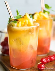 two glasses filled with drinks sitting on top of a cutting board