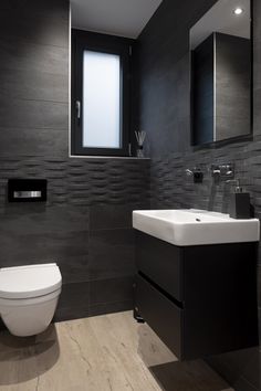 a white toilet sitting next to a bathroom sink under a window in a room with gray walls