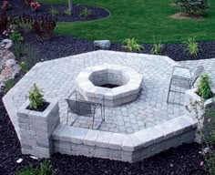 an outdoor fire pit surrounded by black rocks and gravel with chairs around it in the middle