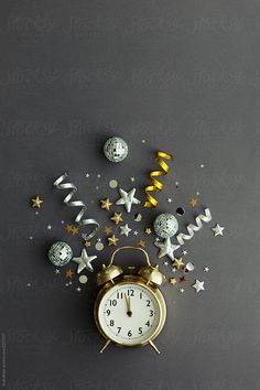 an alarm clock surrounded by stars and confetti on a gray background with gold foil