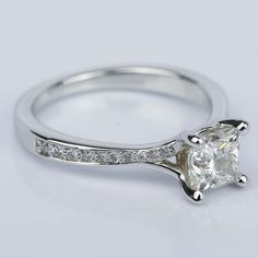 a white gold ring with a princess cut diamond and channel set diamonds on the side