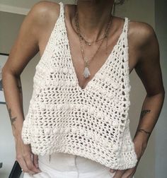 a woman wearing white shorts and a crocheted tank top is posing for the camera