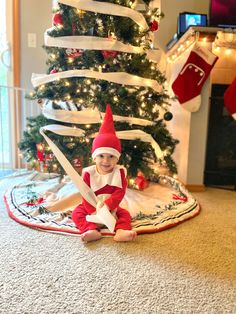 the elf is sitting on the floor in front of the christmas tree