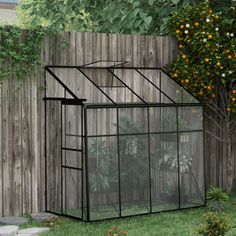 a small black greenhouse sitting in the grass next to a wooden fence and orange trees