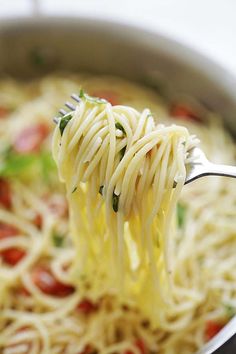 a fork full of spaghetti being lifted from a pot with tomatoes and basil on top