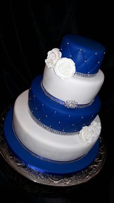 a blue and white three tiered cake on a silver platter with black background