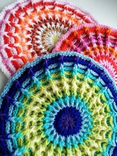 three crocheted plates are sitting on a table top, one is multicolored and the other is white