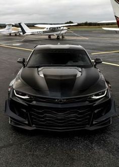 a black chevrolet camaro is parked in front of an airplane on the tarmac