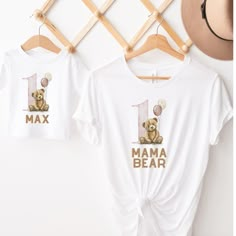 two t - shirts with the number one and a teddy bear on them hanging up