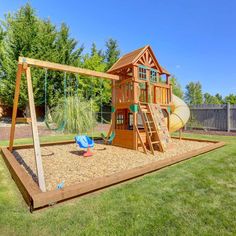 a wooden swing set with a slide and swings in the back yard, surrounded by grass