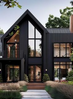 a large black house with lots of windows and plants on the front lawn, along with steps leading up to it