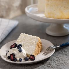 a piece of cake on a white plate with blueberries and whipped cream next to it