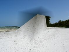 a skateboarder doing a trick on the side of a white wall with trees in the background