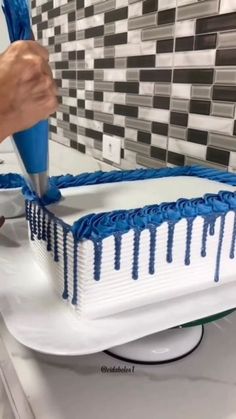 a person is cutting into a cake with blue icing on the top and white frosting on the bottom