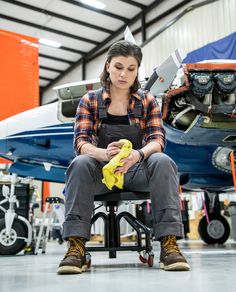 a woman is sitting on a chair in front of an airplane and looking at something